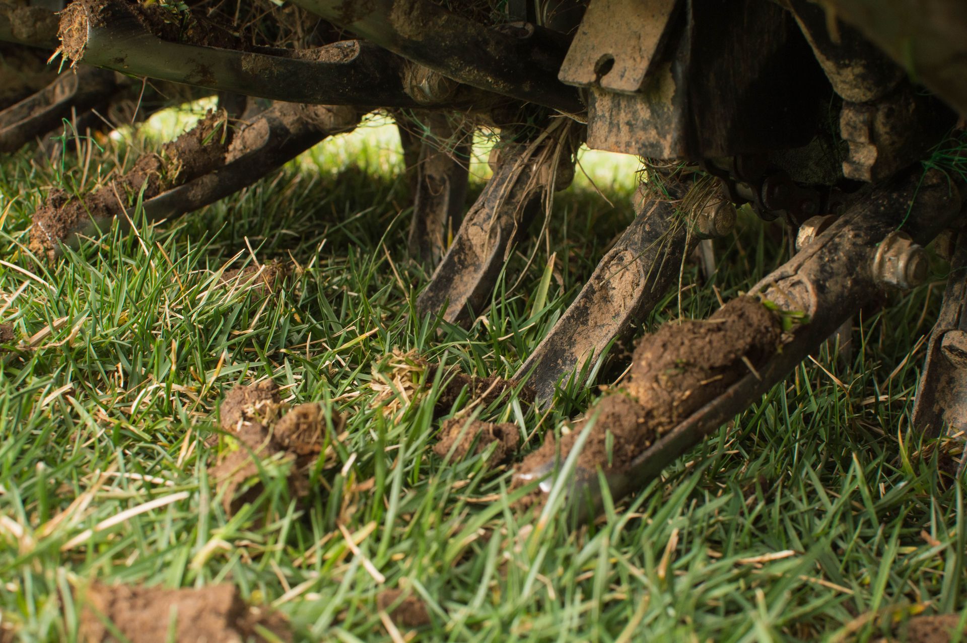 Close-up of muddy wooden cart wheels in grass, with rusted metal parts and soil debris