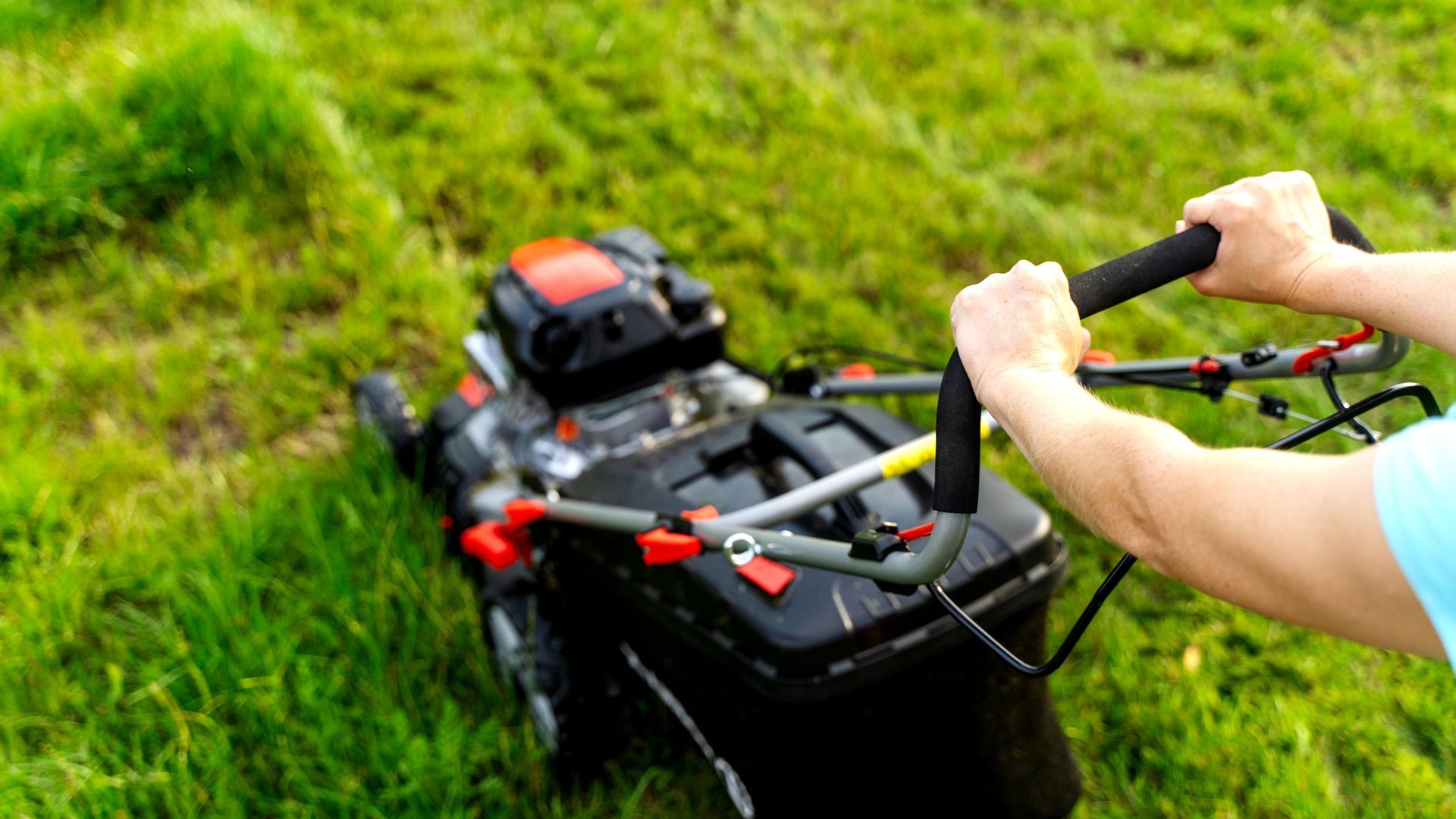 Person pushing a lawn mower on a grassy slope outdoors.