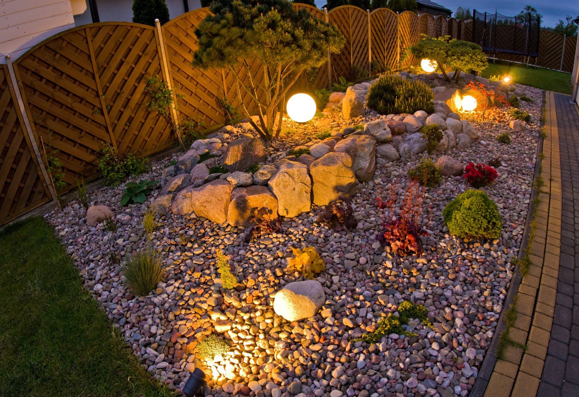 Curved stone path through a colorful landscaped garden with green grass and red-orange flower beds