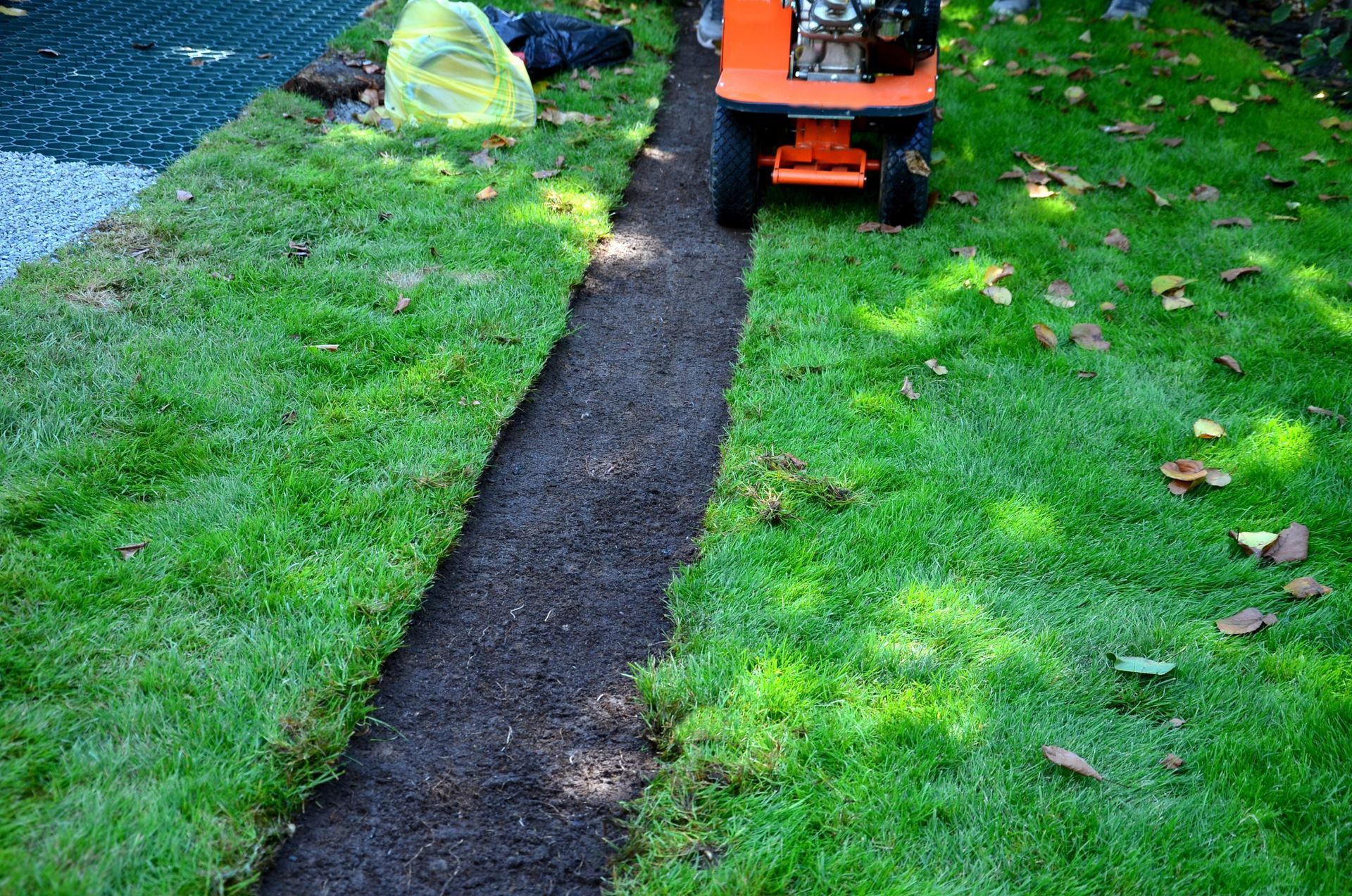 Orange lawn mower on a narrow black path through green grass