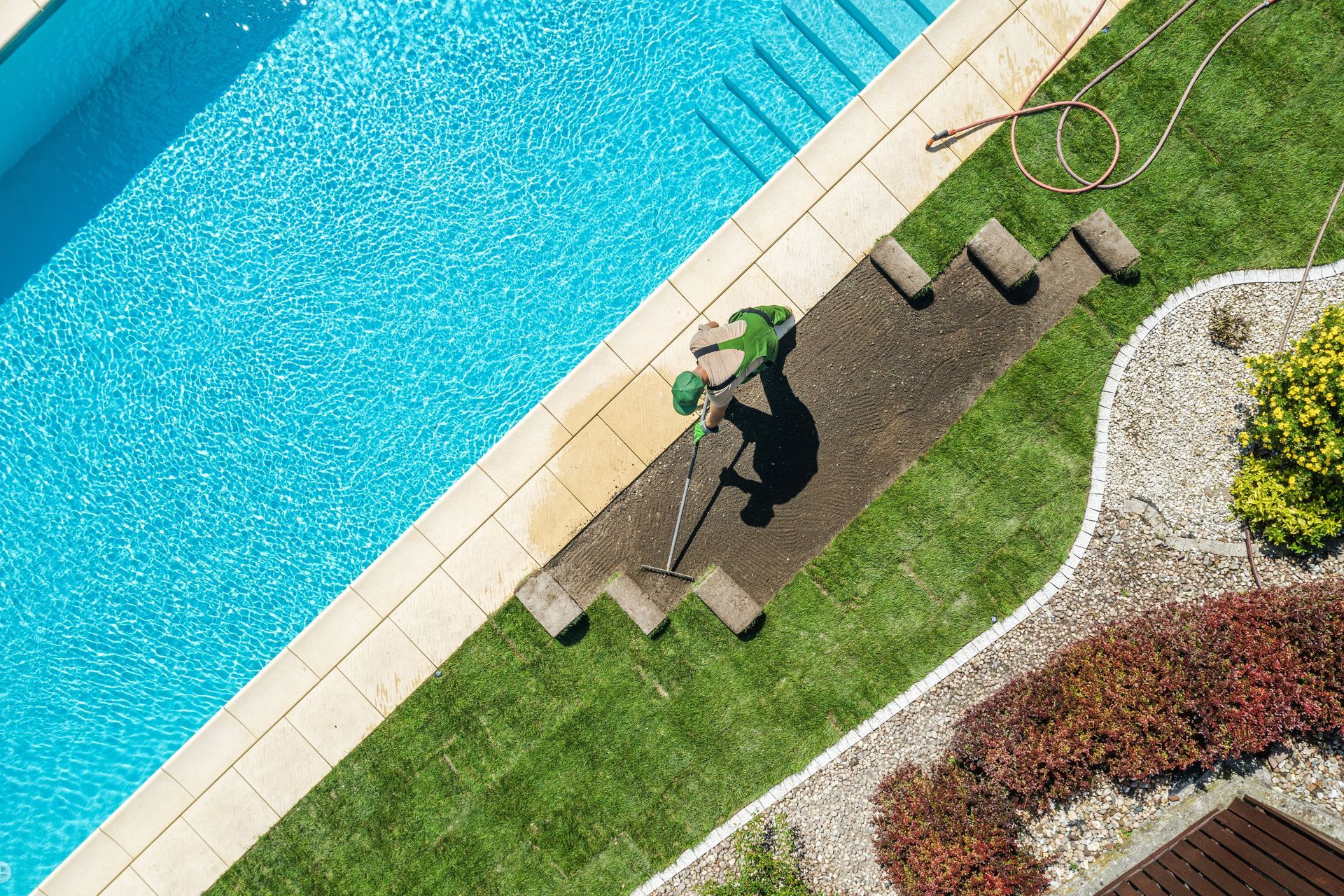 Person standing by a turquoise pool on a stone path beside a green lawn