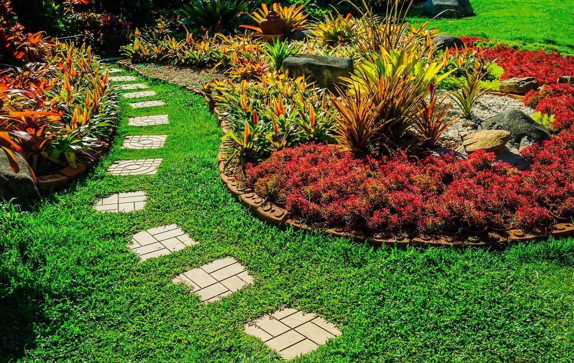Curving stone path through a lush garden with colorful red, orange, and yellow plants