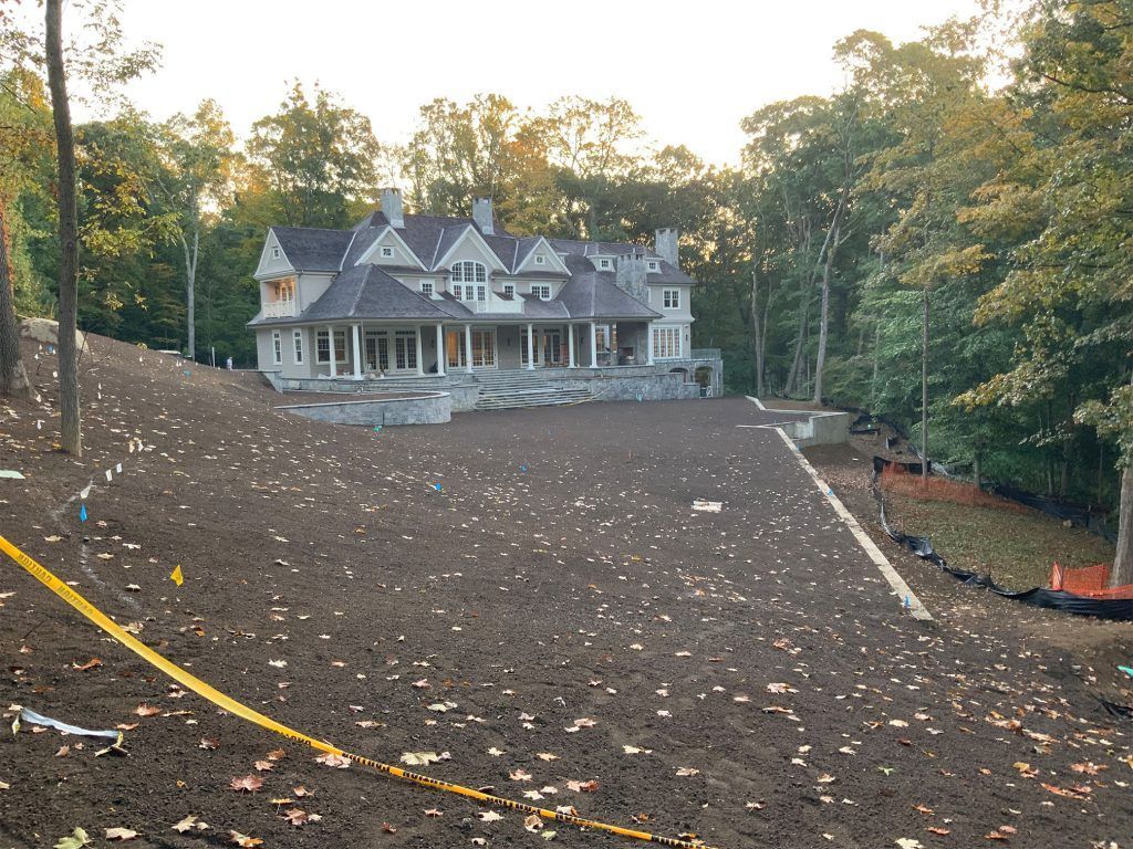 Large gray house on a steep, cleared hillside surrounded by trees at sunset