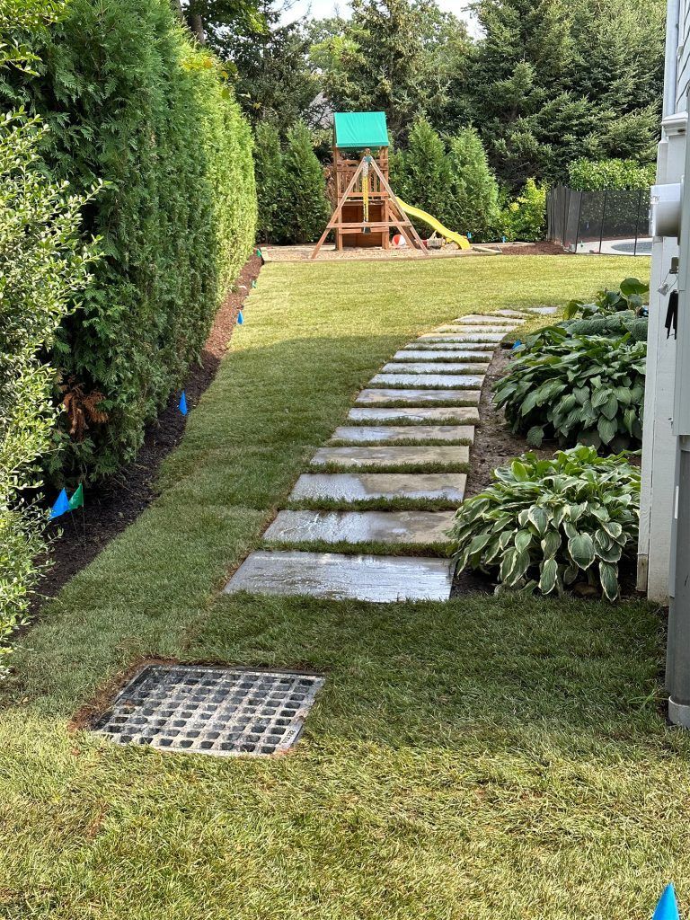 Backyard path with stepping stones, hedge, and a wooden playset in the distance