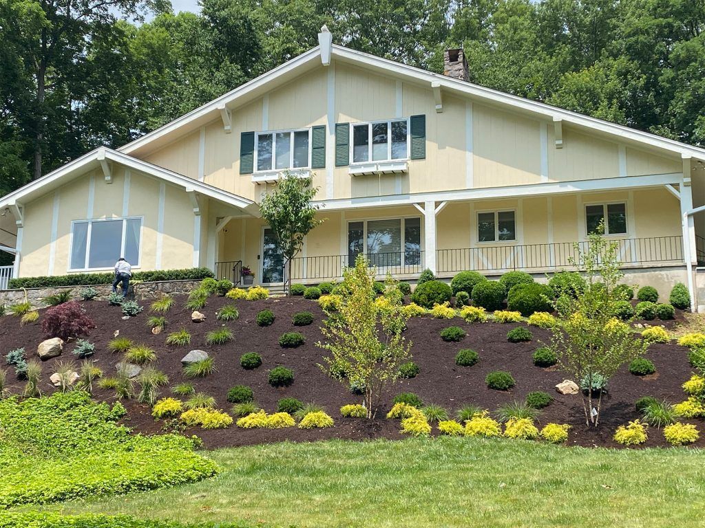 Beige house with white trim and a landscaped front yard on a sloped lawn