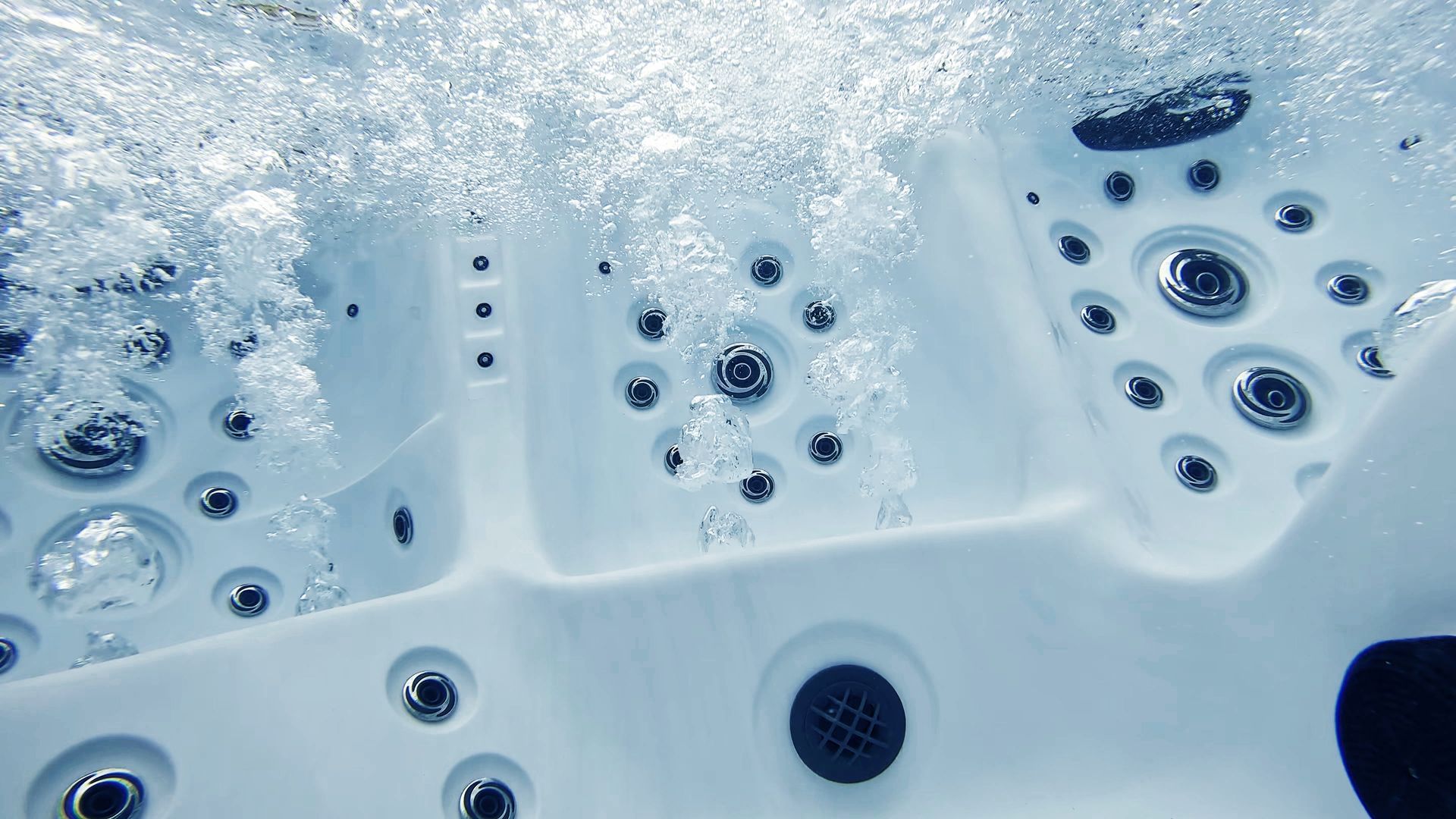 White bubbling hot tub jets and controls with water ripples across the spa surface