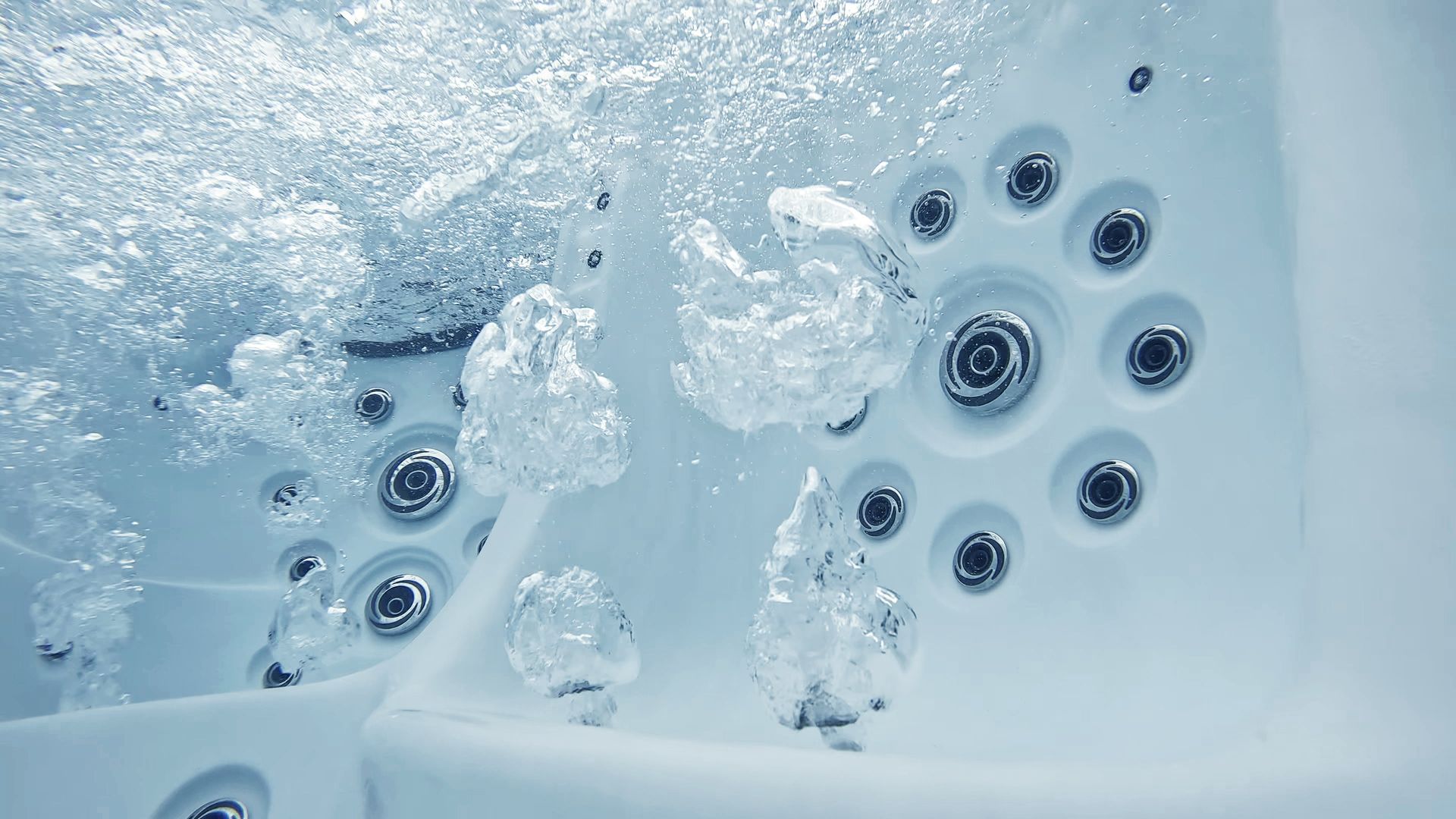 White bathtub with water jets bubbling around submerged silver nozzles in pale blue water