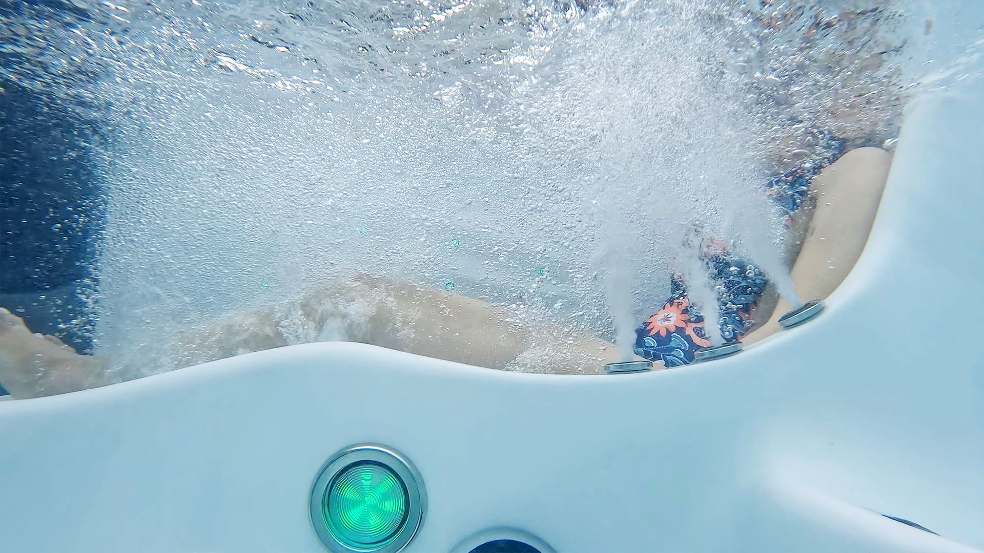Person splashing in a white jacuzzi, with bubbles and a glowing green jet button in front.