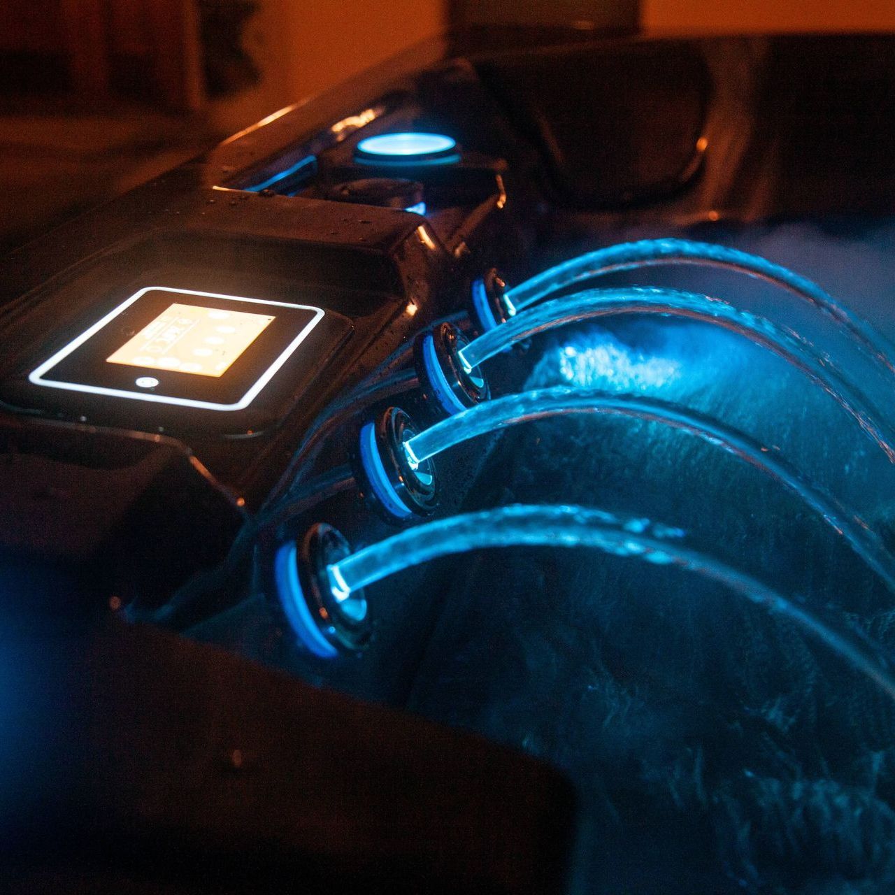 View of a hot tubs jet waterfall at night with blue glowing light.