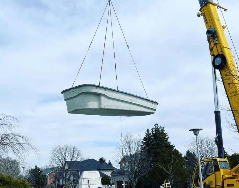 Pool Install in progress with a crane lifting it into a backyard over a house