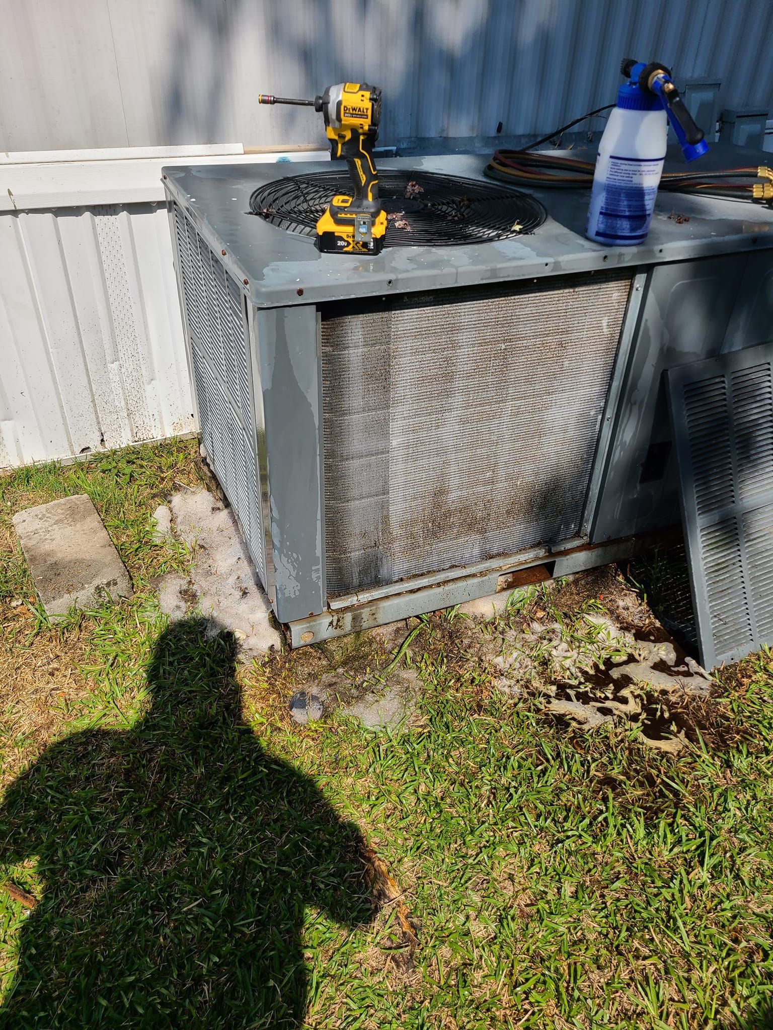 An air conditioner unit with tools on top, outdoors, grass, and a person's shadow.