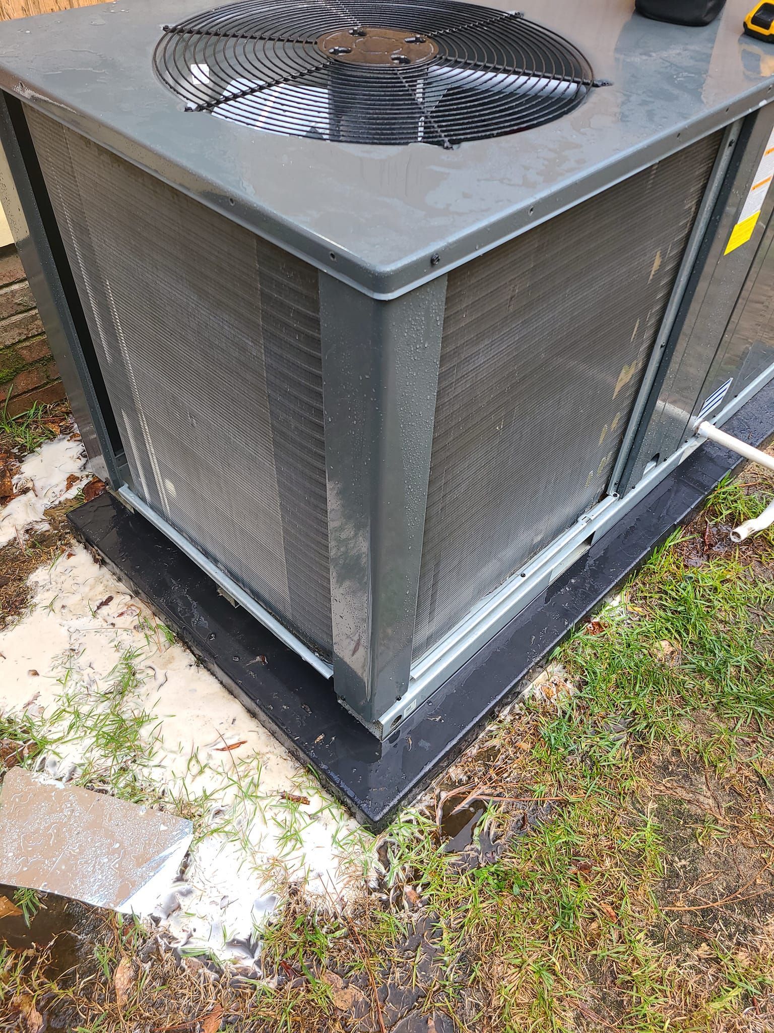 An outdoor air conditioning unit with a top fan and side cooling coils on a black pad.