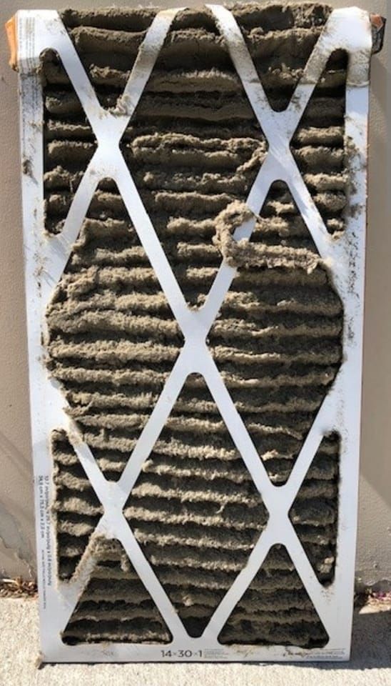 Dirty HVAC air filter, covered in dust and debris, white frame.