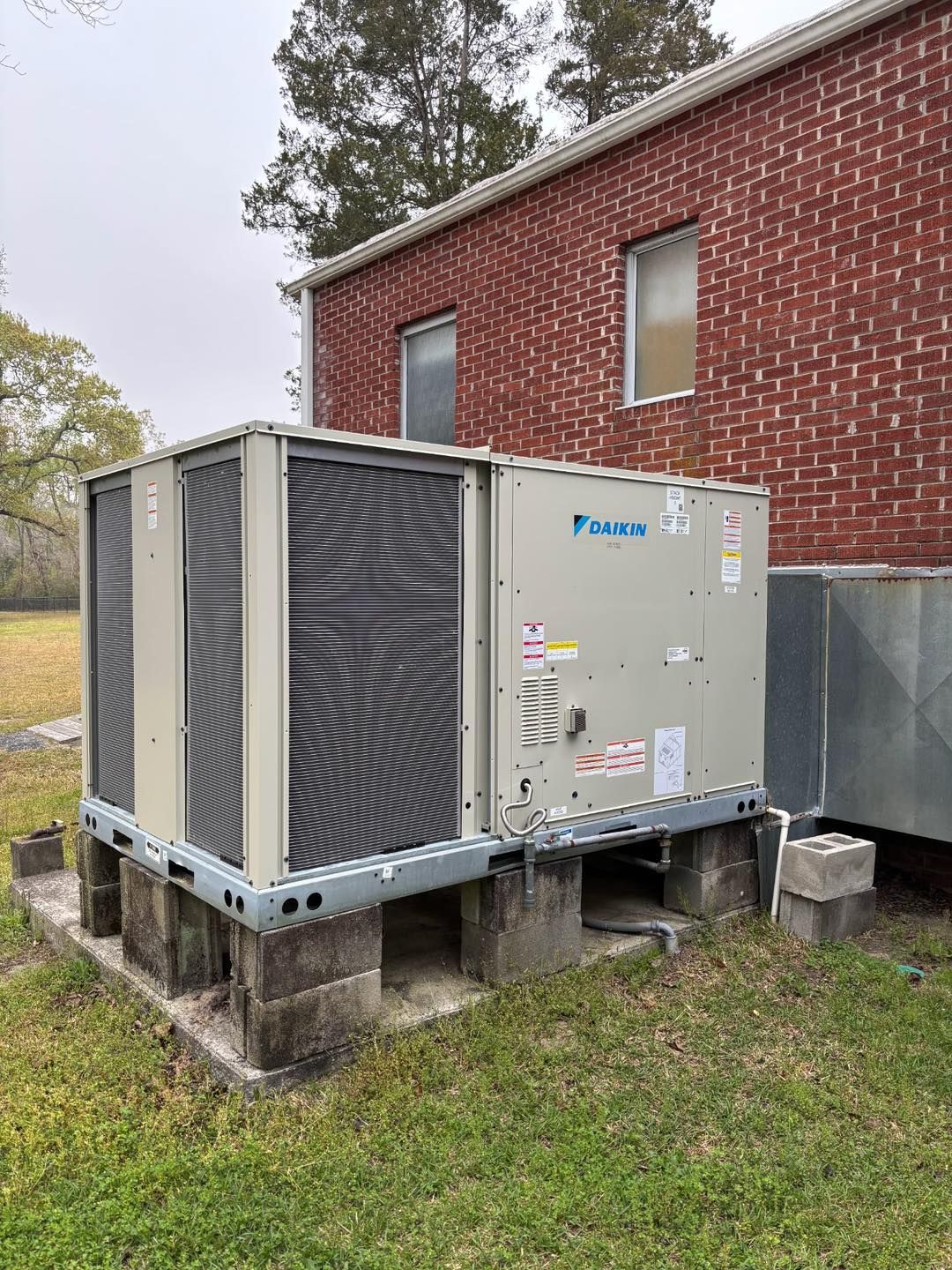 An air conditioning unit outdoors, against a brick building.