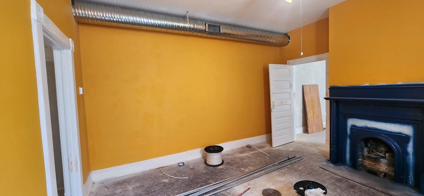 A room under renovation with yellow walls, a blue fireplace, and an exposed duct.