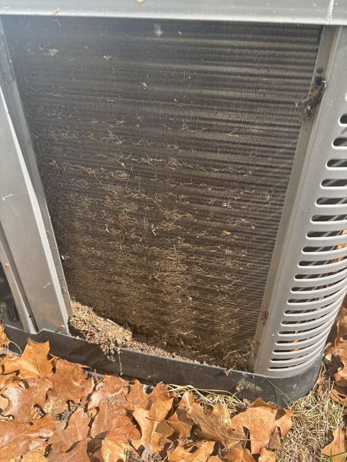 Dirty air conditioning unit with debris blocking the coils. Outdoor setting with fallen leaves.