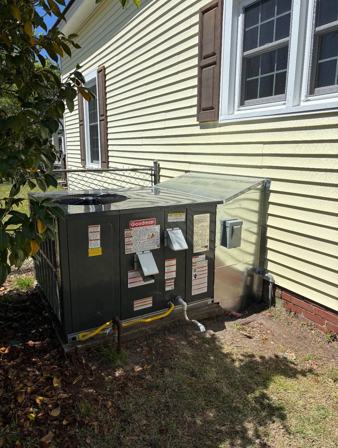 AC unit next to a yellow house with brown shutters. Unit is on grass.