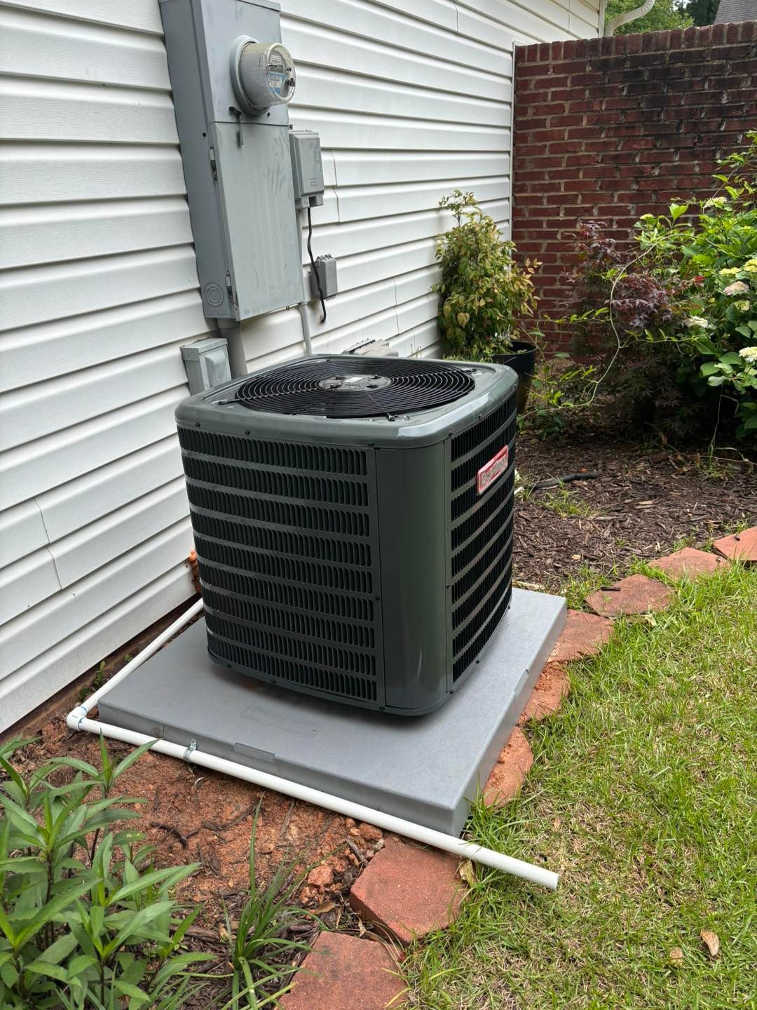 Air conditioning unit on a concrete pad next to a house and electrical box.