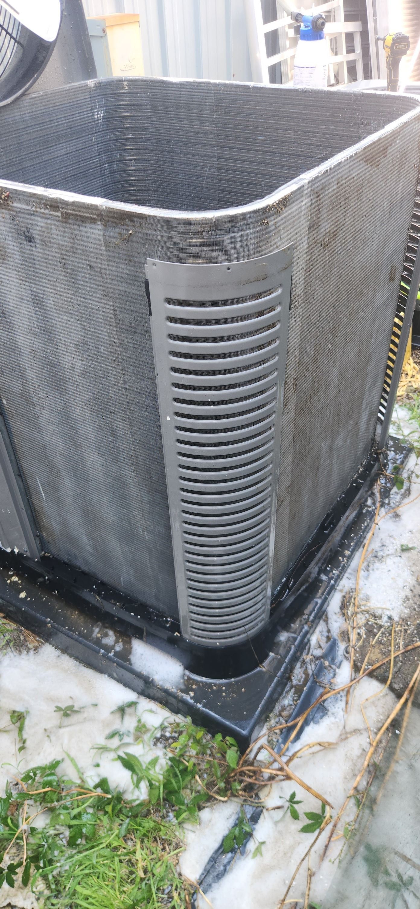 Black outdoor air conditioning unit with side vent, snow and grass.