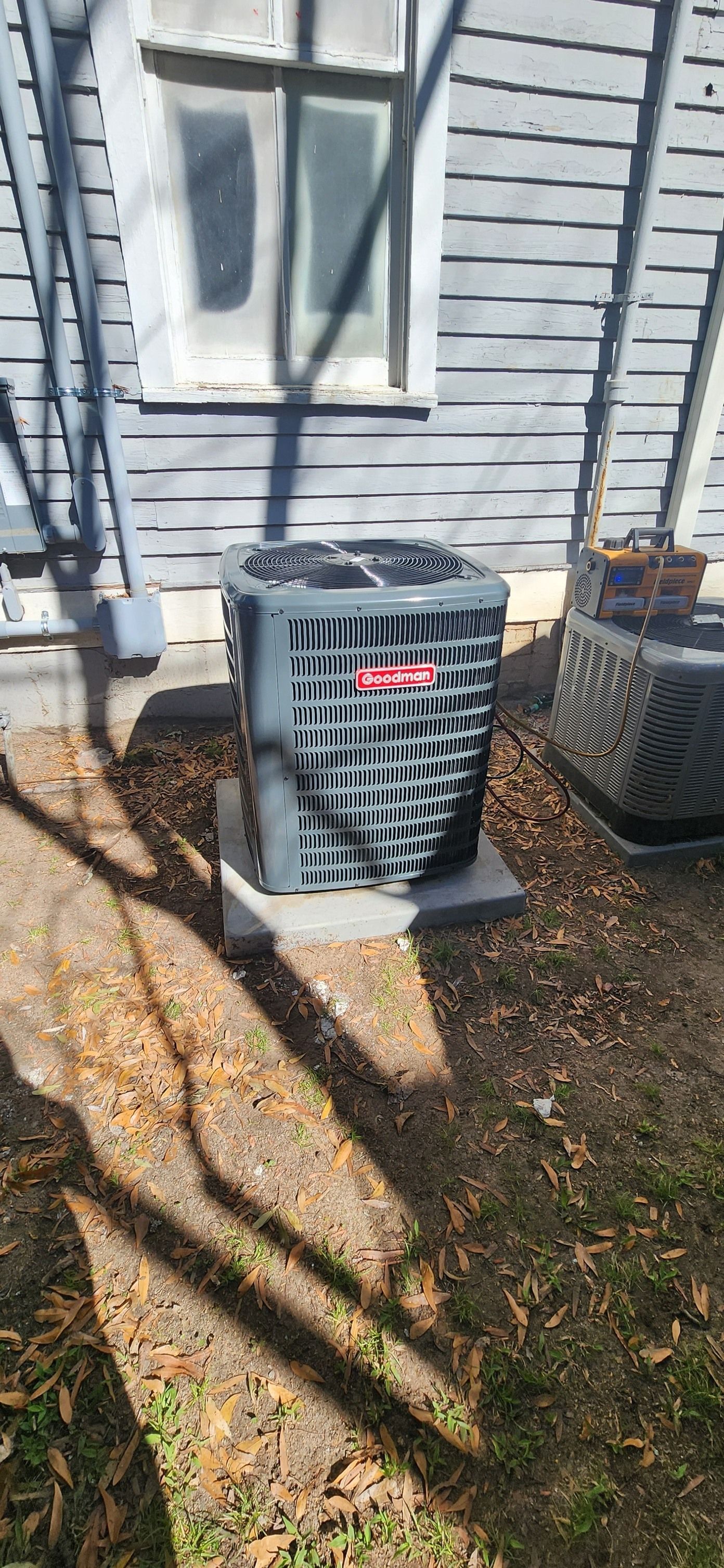 An outdoor air conditioning unit sits on a concrete pad near a building with gray siding.