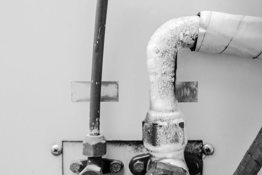 Insulated white pipe and dark vertical pipe mounted on a wall with metal brackets and valves