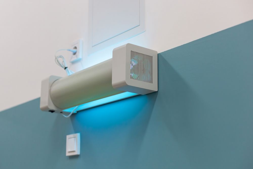 Wall-mounted air curtain above a teal wall, glowing blue underneath with a small control box below.