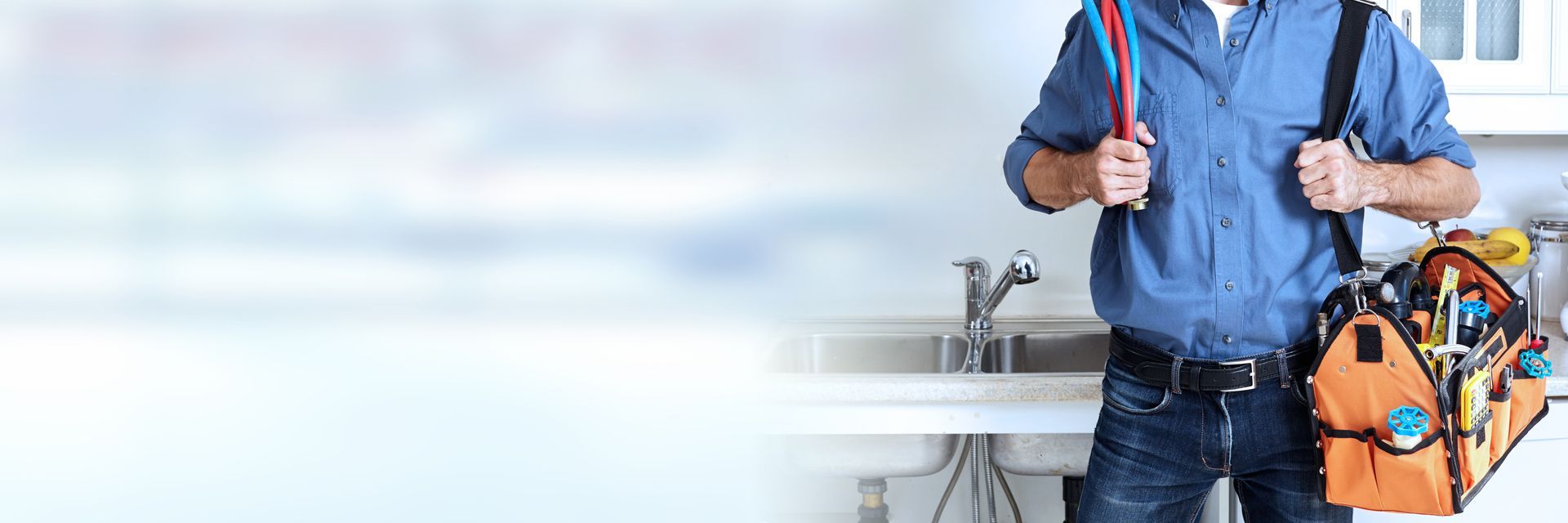Person holding pipes and a tool bag beside a kitchen sink with copy space. Person holding pipes and a tool bag beside a kitchen sink with copy space.