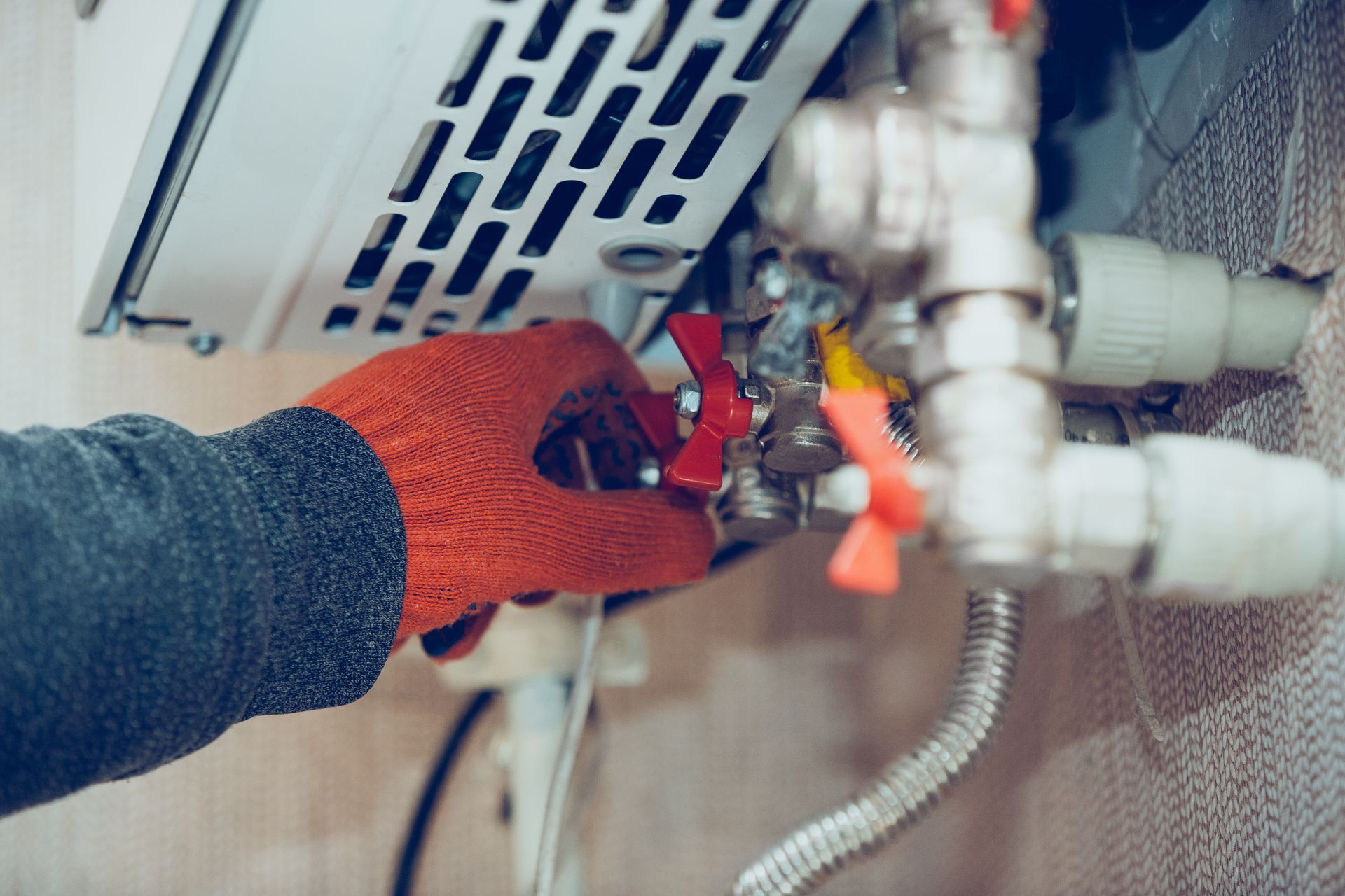 Gloved hand tightening plumbing valves beneath a sink with exposed pipes