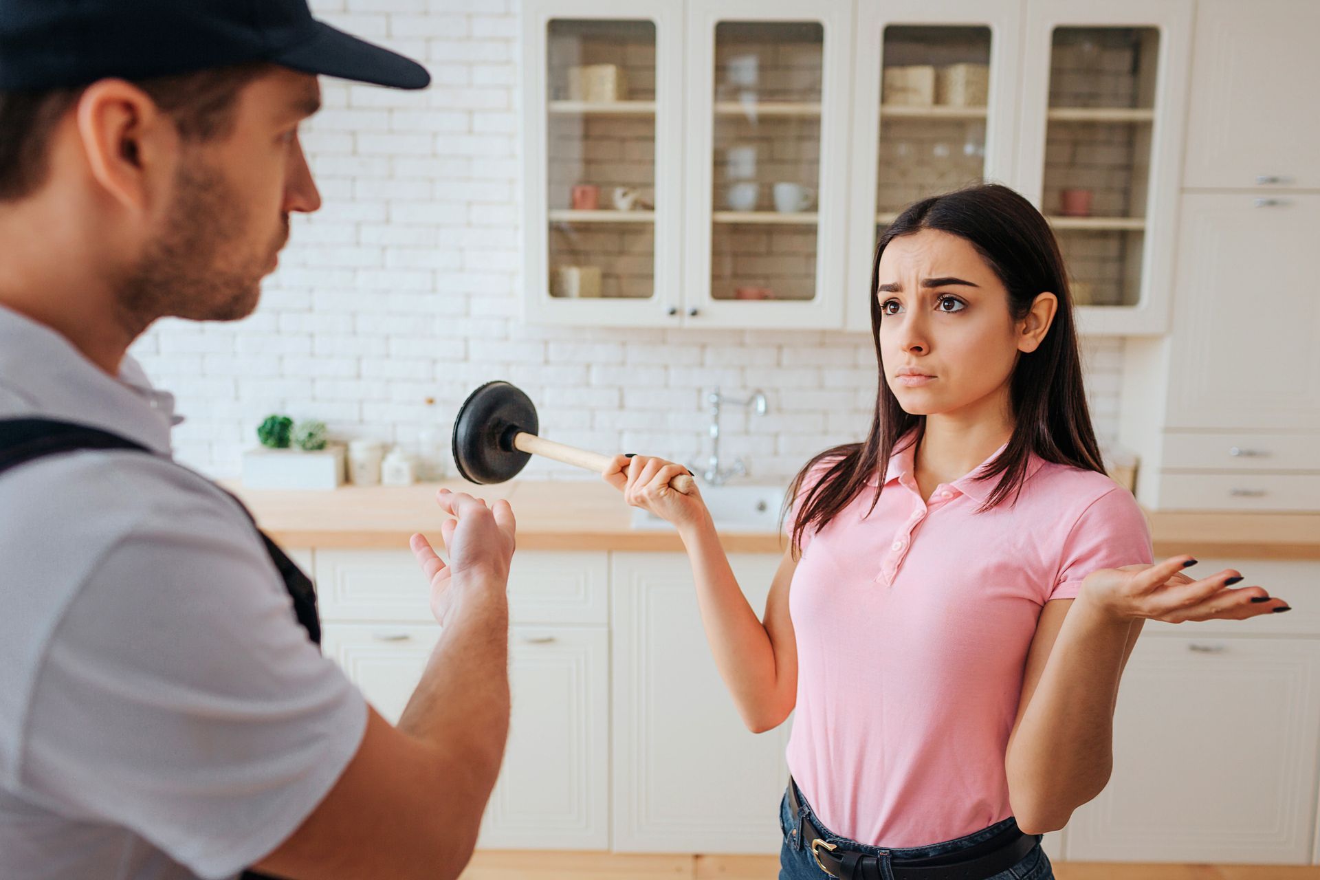 Woman with plunger consulting plumber in modern kitchen about clogged sink plumbing issue. Woman with plunger consulting plumber in modern kitchen about clogged sink plumbing issue.