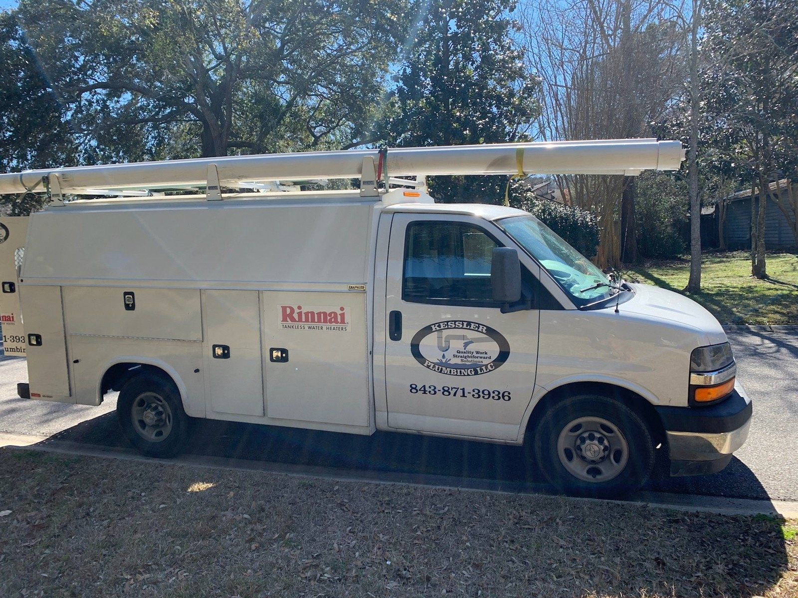 White work van with logo and ladder rack parked on the street.