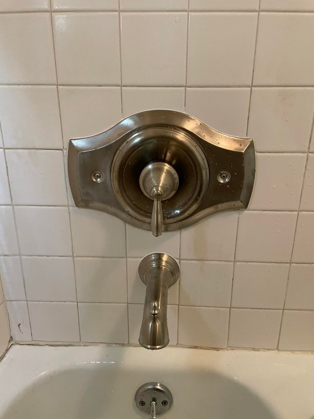Brushed nickel shower fixture and faucet on white tiled wall above a bathtub.