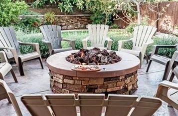 Eight outdoor chairs circle a lit fire pit in a backyard.
