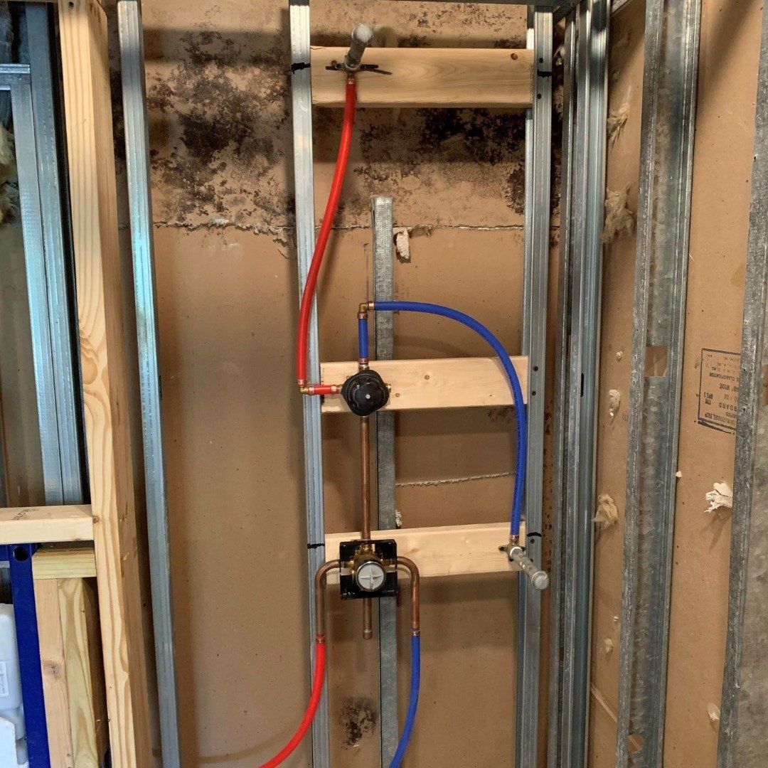 Piping system with red and blue pipes in a wall, likely for a shower. Metal framing and wooden supports are visible.