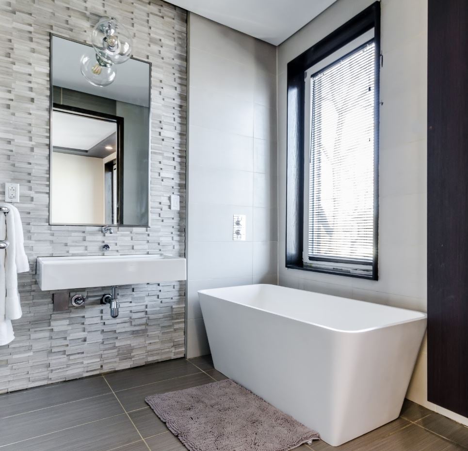 Modern bathroom with a white tub, stone accent wall, and large window.
