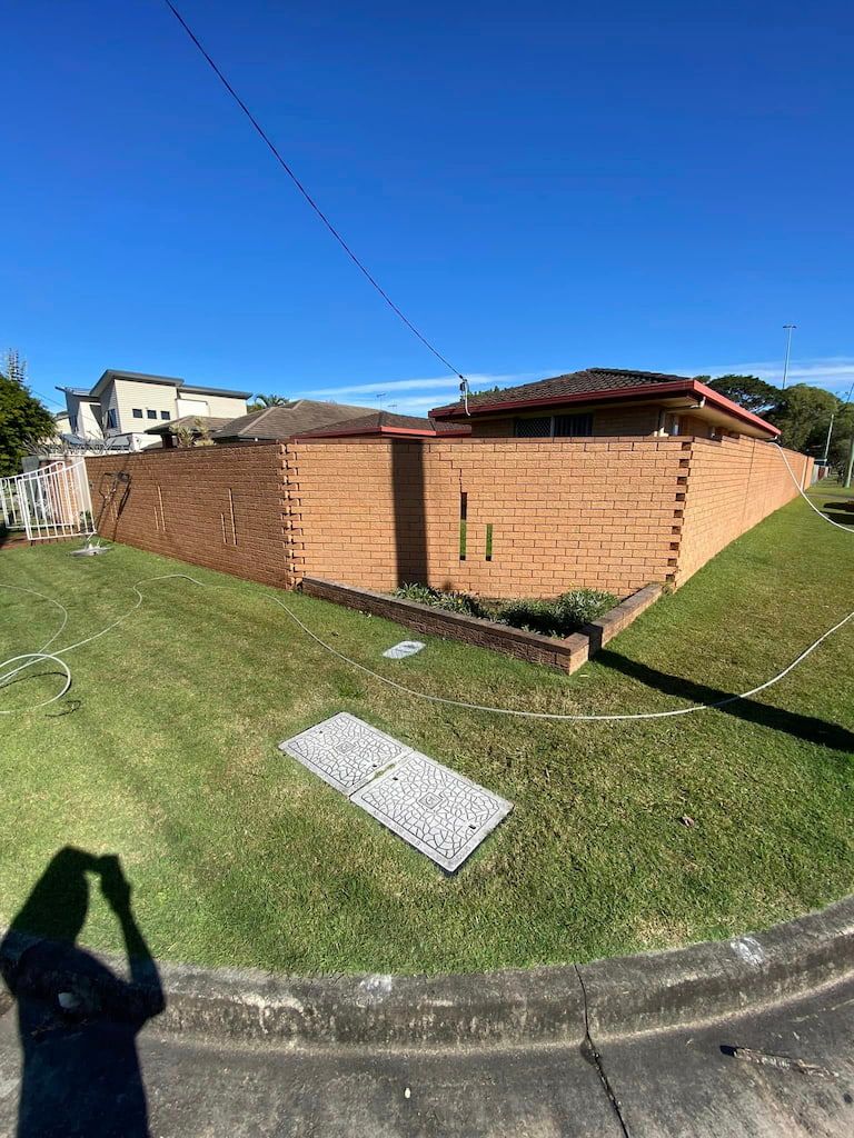 a pressure cleaned brick wall is surrounded by a lush green lawn on the gold coast