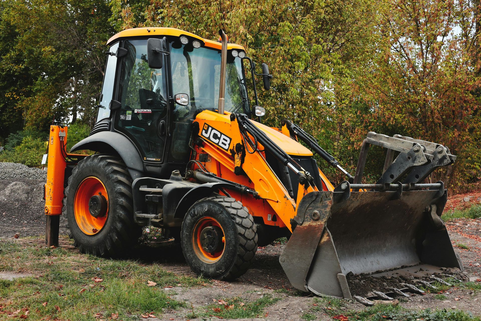 Yellow and black JCB backhoe loader parked on a construction site with trees in the background.