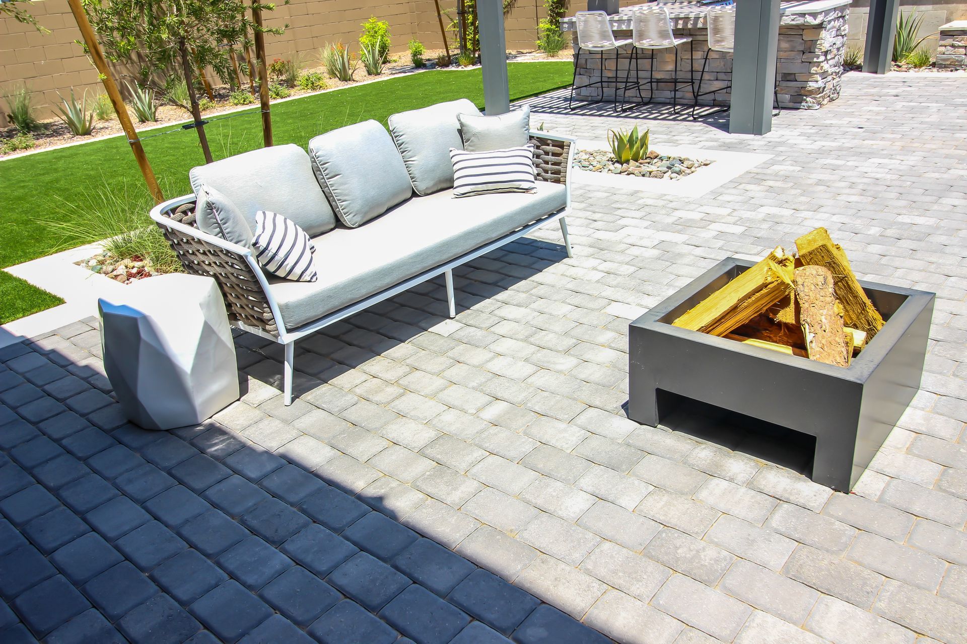 Outdoor patio with couch, fire pit, and stone side table on brick pavers.