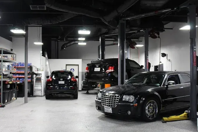 Interior of an auto repair shop with cars on lifts and in bays; black and silver vehicles.