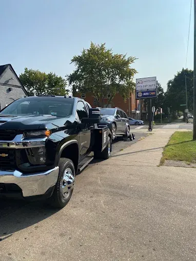 Black tow truck towing a silver car on a sunny city street.