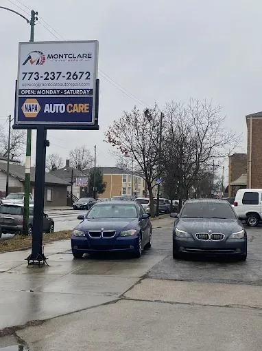 Two BMW cars parked in front of Montclare Auto Care sign on a wet street.
