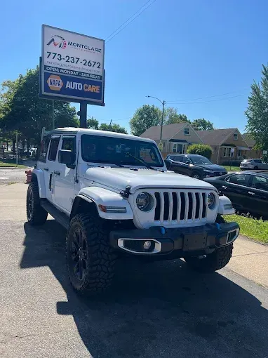 White Jeep Wrangler parked in front of an auto repair shop sign on a sunny day.