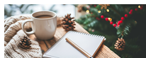 Mug of coffee next to a notepad and pen, cozy with a knitted blanket, pine cones and a Christmas tree.