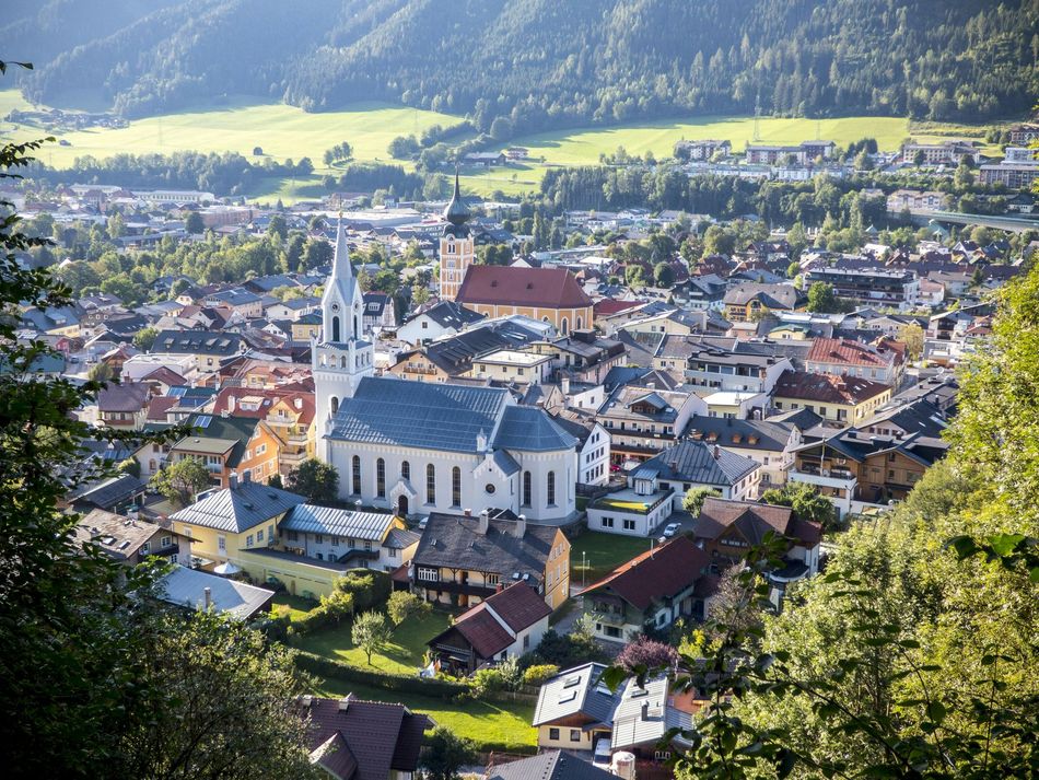 Aerial view of a mountain town with a white church and red-roofed buildings in a green valley