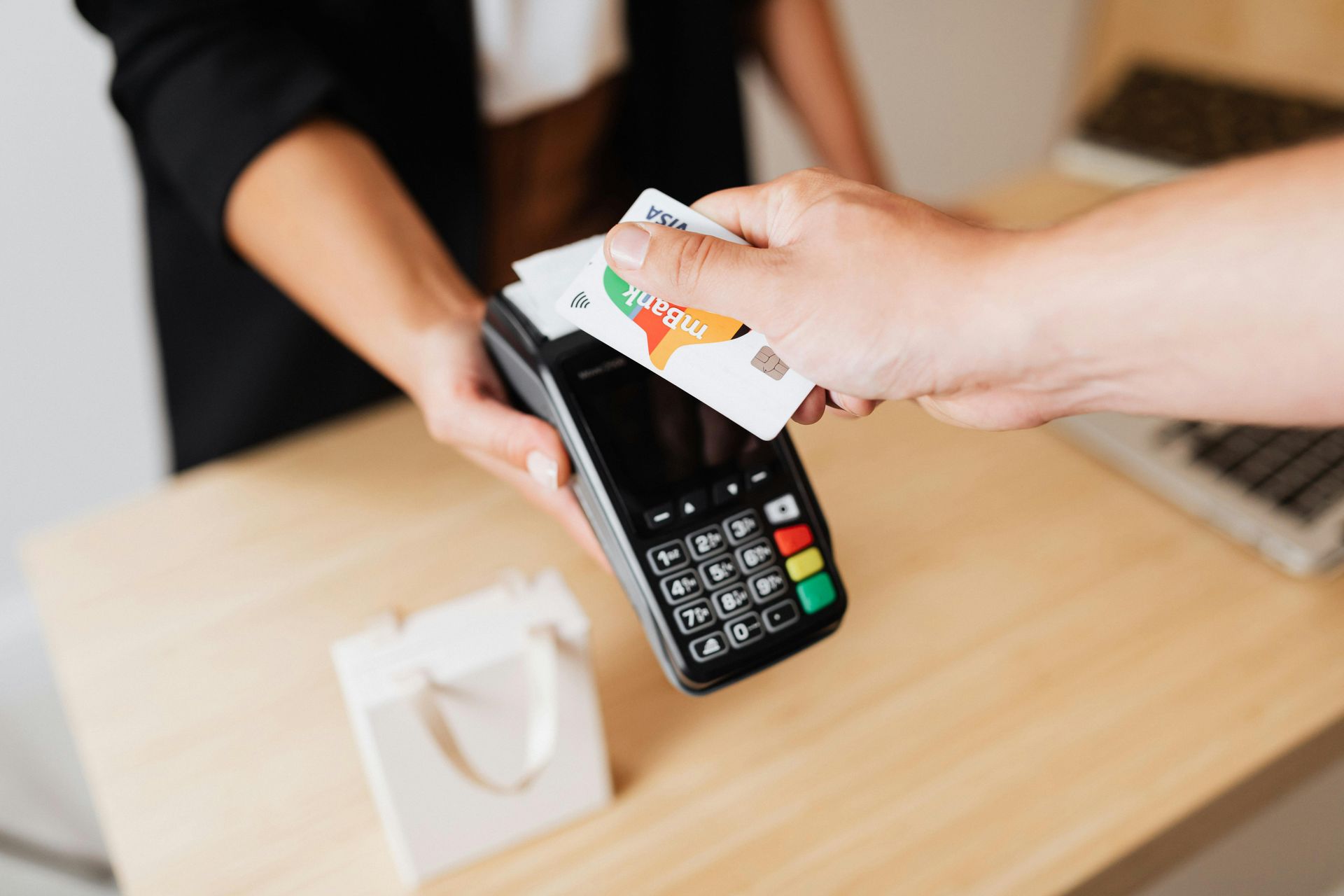 Hand holding a credit card over a payment terminal at a checkout counter