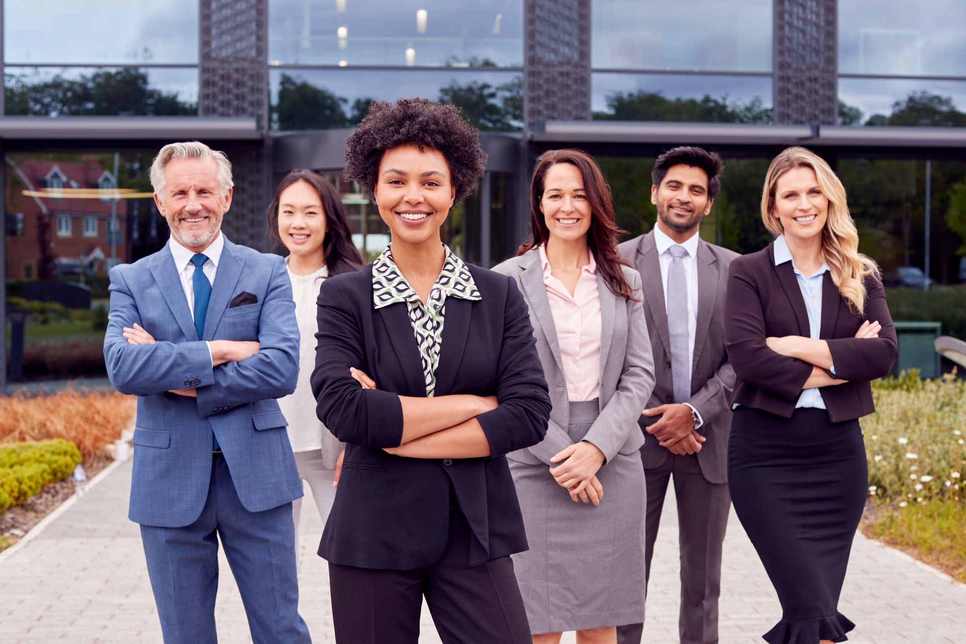 Group of businesspeople, arms crossed, smiling in front of a modern building.