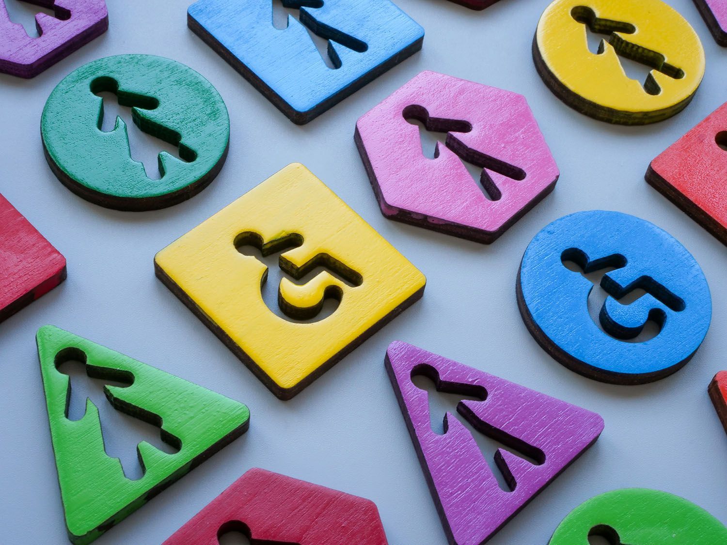 Colorful wooden shapes with cut-out disability access symbols: person walking and wheelchair symbols.