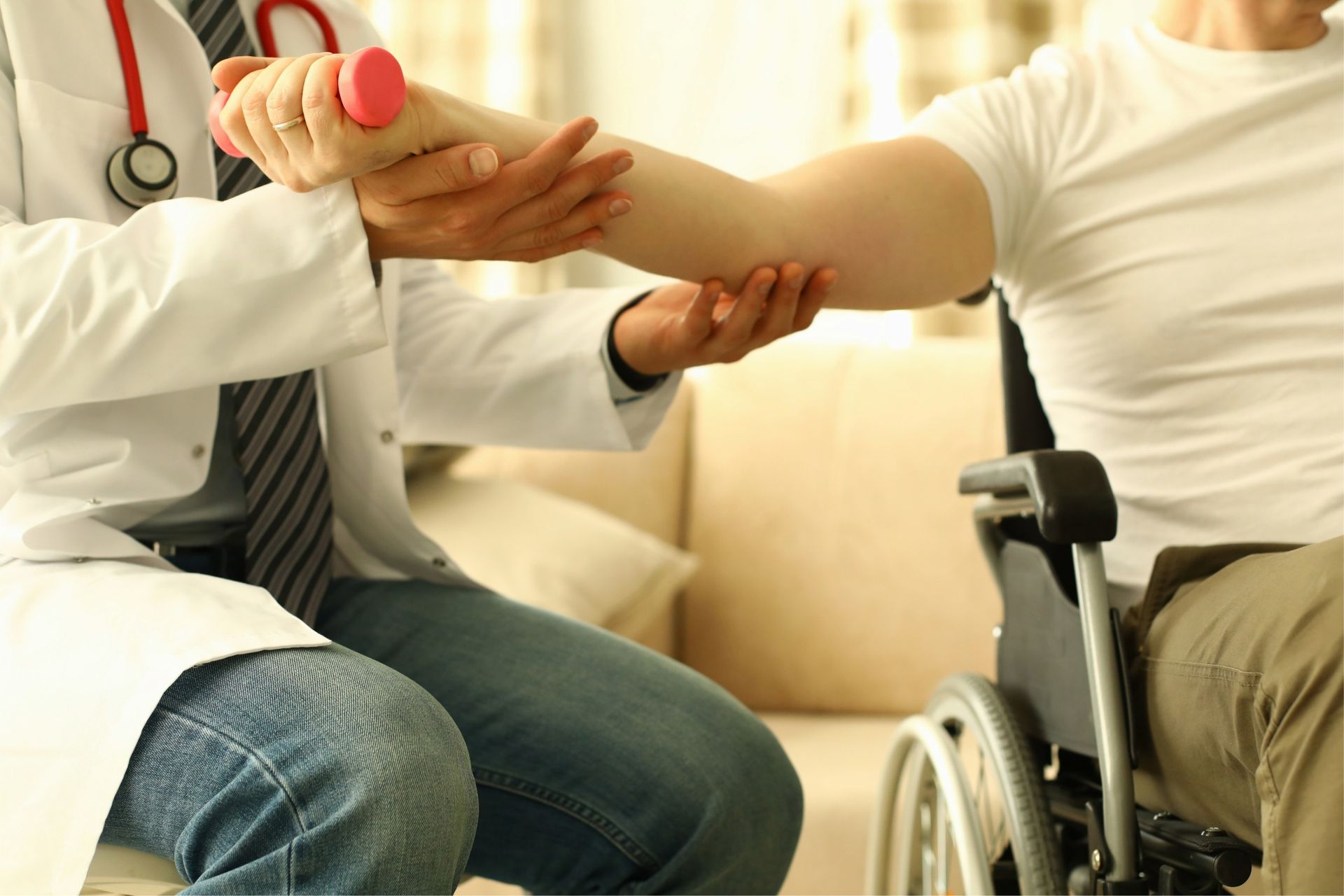 Doctor examining patient's arm, seated in a wheelchair. Medical exam in a room.