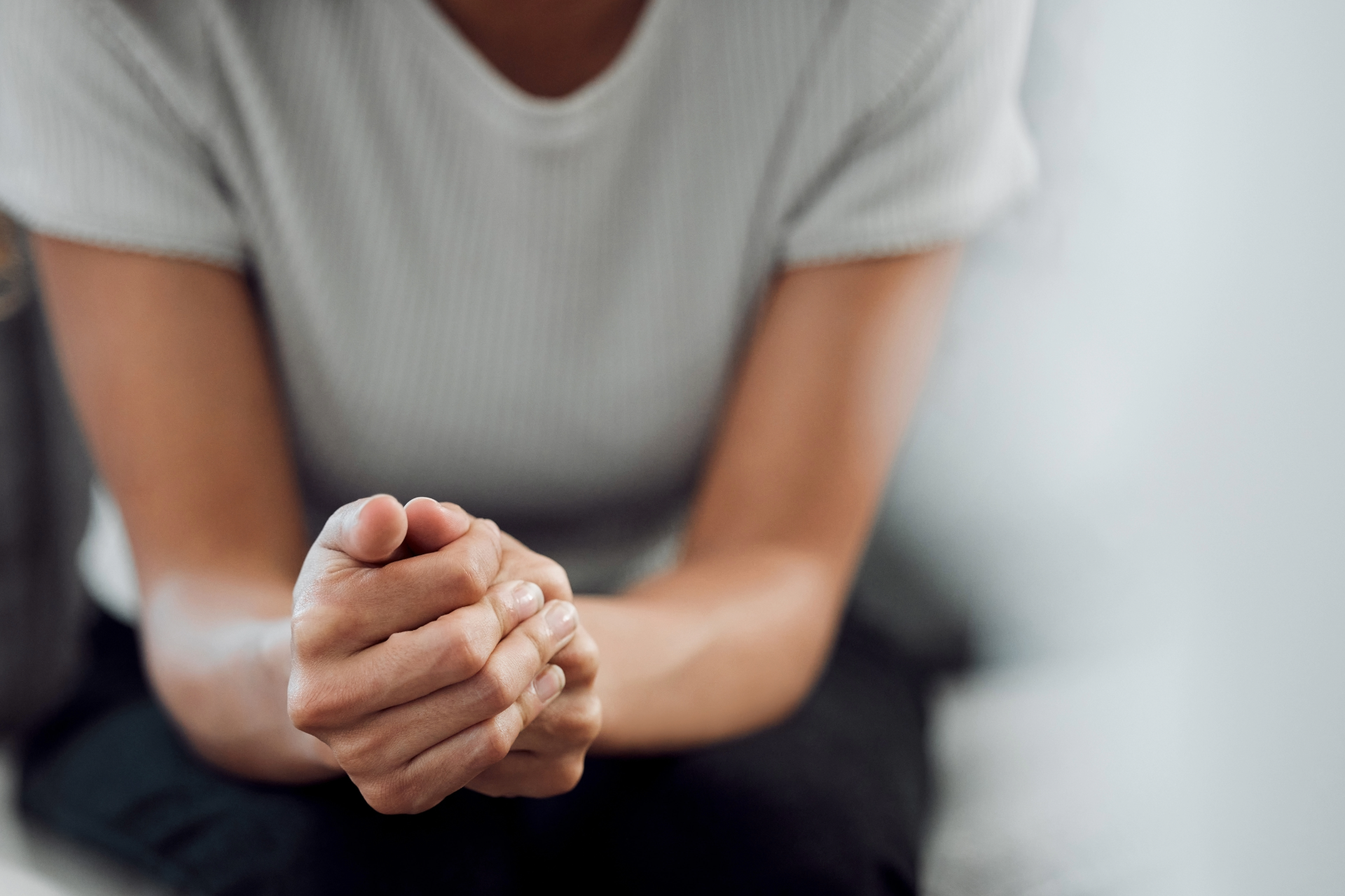 Person with clasped hands wearing a white shirt, seated against a blurred background.