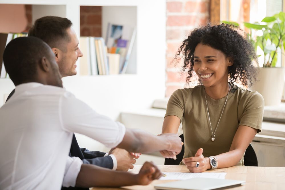 A man and a woman are shaking hands while sitting at a table.