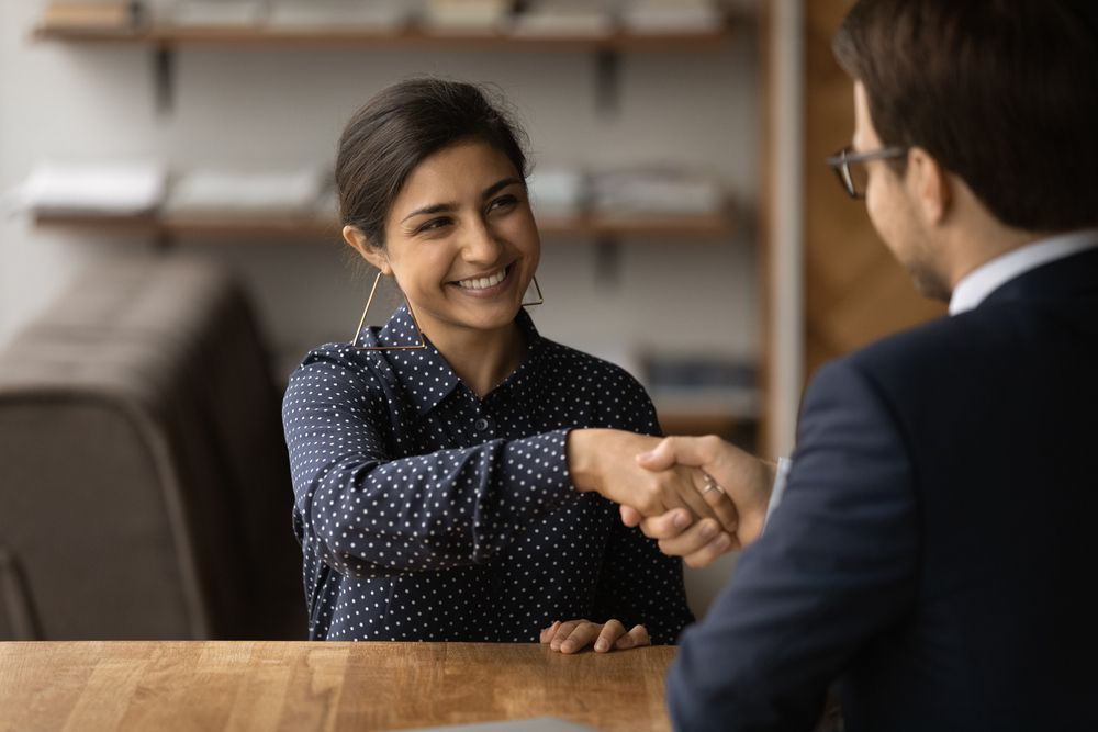 A woman is shaking hands with a man during a job interview.